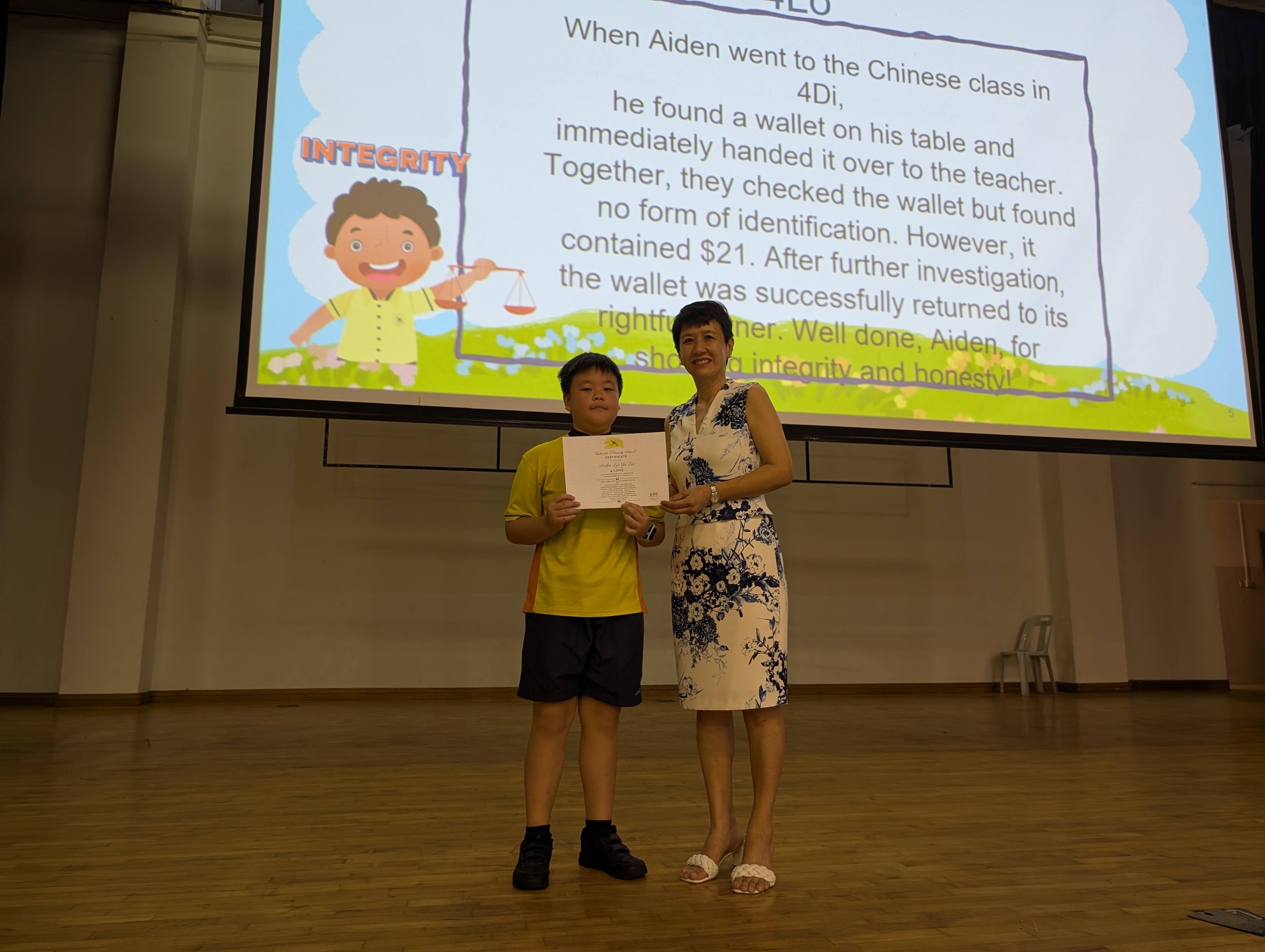 Aiden receiving his certificate from Mrs Liang on stage as they pose for a photo